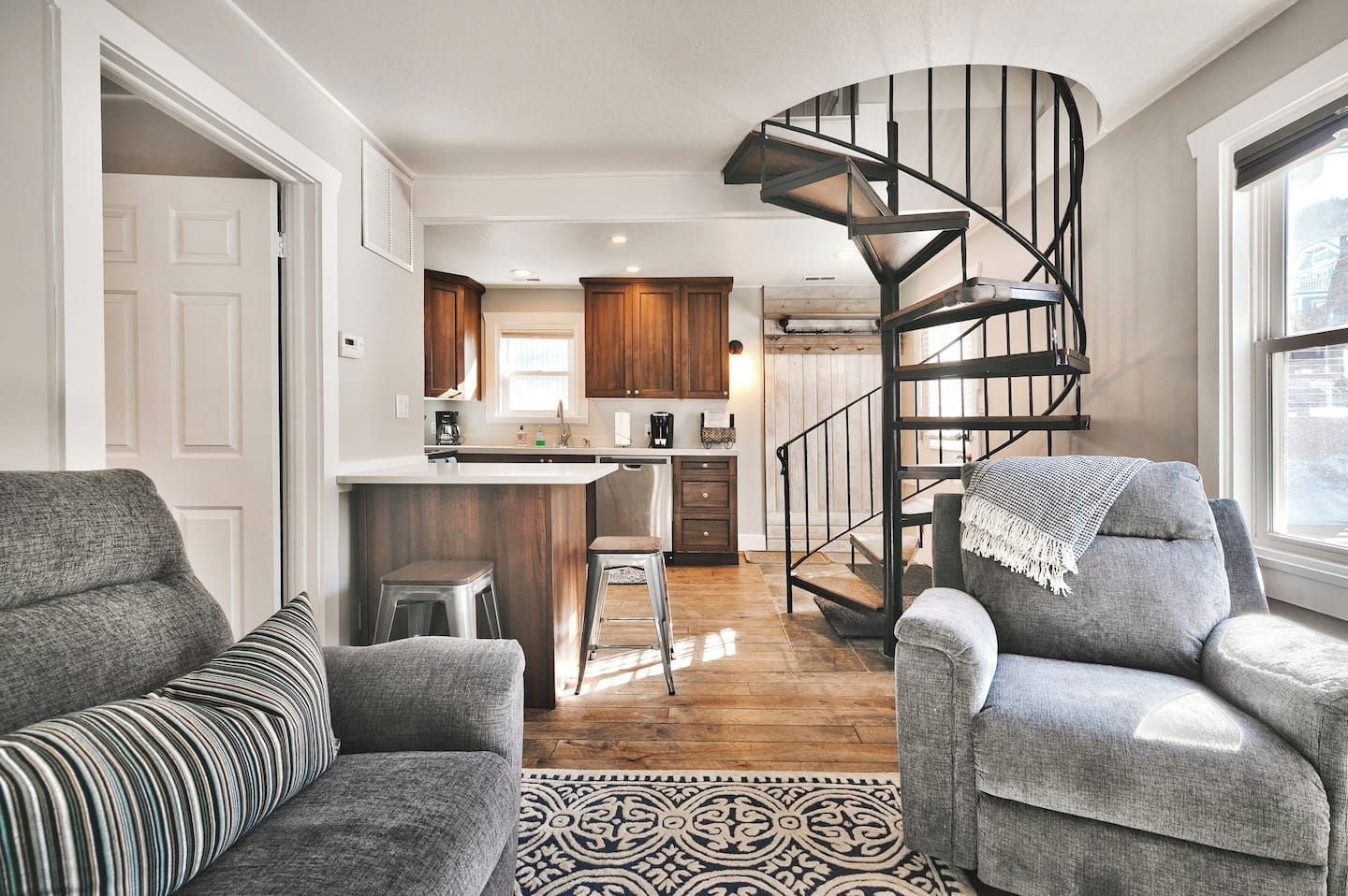 Un interior moderno con una escalera espiral, una cocina con armarios de madera y una zona de estar con dos sofás.