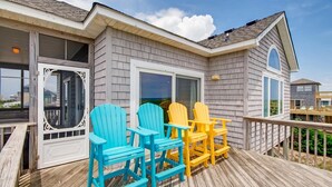 A wooden deck with four Adirondack chairs in blue and yellow colors, a white door, and a window. - Oceanfront Home in Waves w/ Private Pool, Hot Tub, Game Room. Total Seaduction. (Waves)