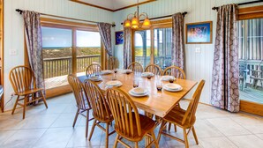 A dining area with a wooden table and chairs, large windows with curtains, and a view of the beach. - Oceanfront Home in Waves w/ Private Pool, Hot Tub, Game Room. Total Seaduction. (Waves)