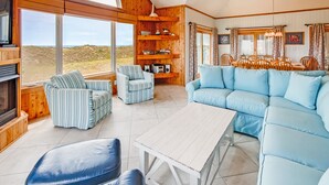 A cozy cabin interior with a large dining table, striped chairs, a blue sofa, and a fireplace. - Oceanfront Home in Waves w/ Private Pool, Hot Tub, Game Room. Total Seaduction. (Waves)