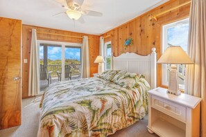 A bedroom with a bed, a nightstand, a ceiling fan, and a view of the outdoors.