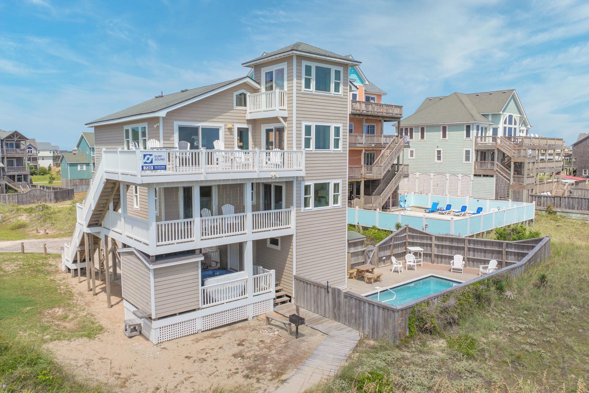 A multi-story beachfront property with a pool, outdoor seating, and a lifeguard tower.