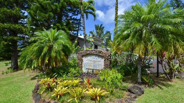 Un complexe hôtelier tropical avec un panneau en pierre, une végétation luxuriante et des palmiers.