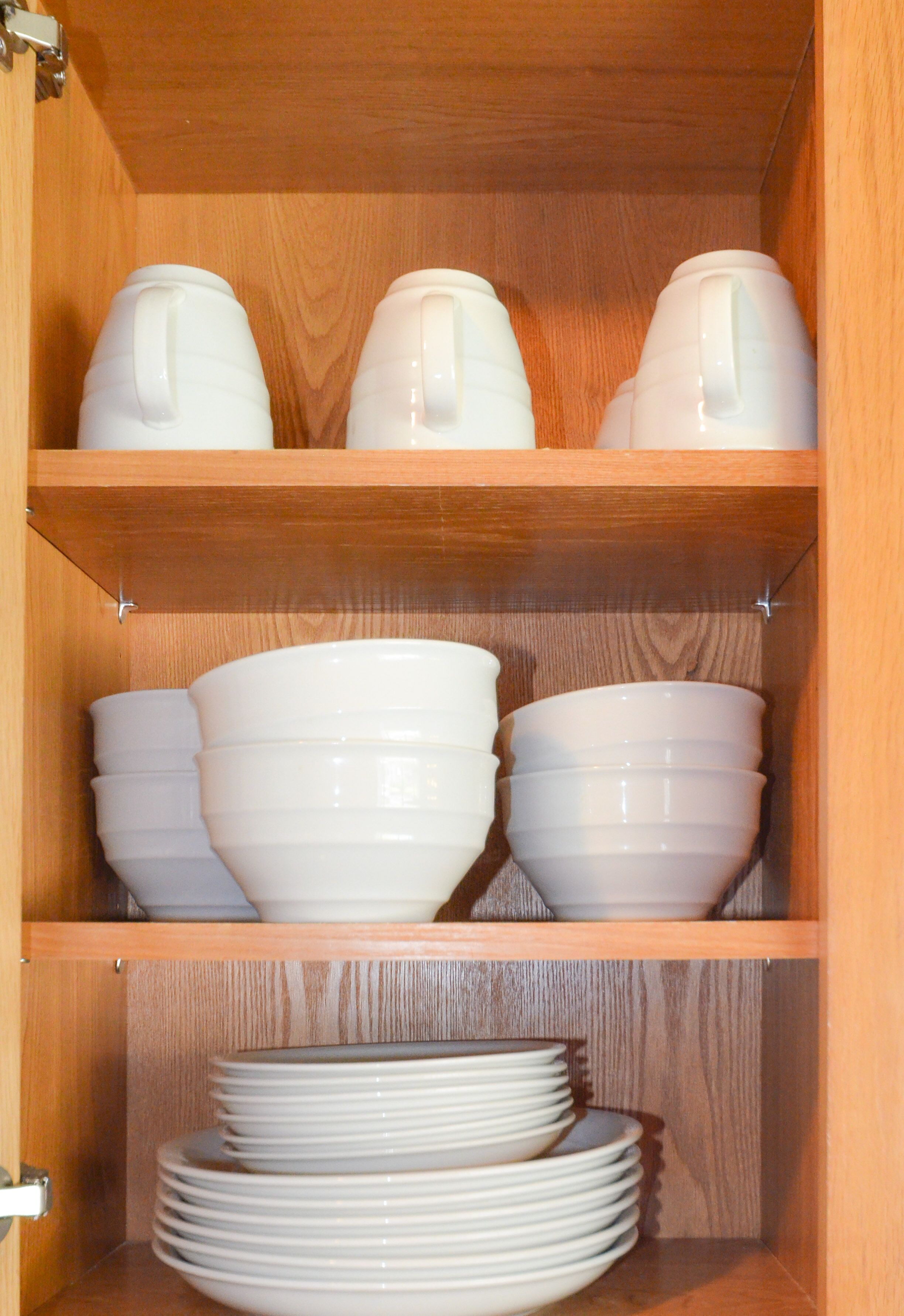 A wooden cabinet with shelves holding white bowls and plates.