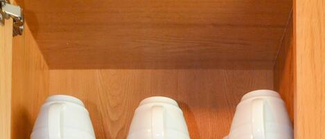 A wooden cabinet with shelves holding white bowls and plates.