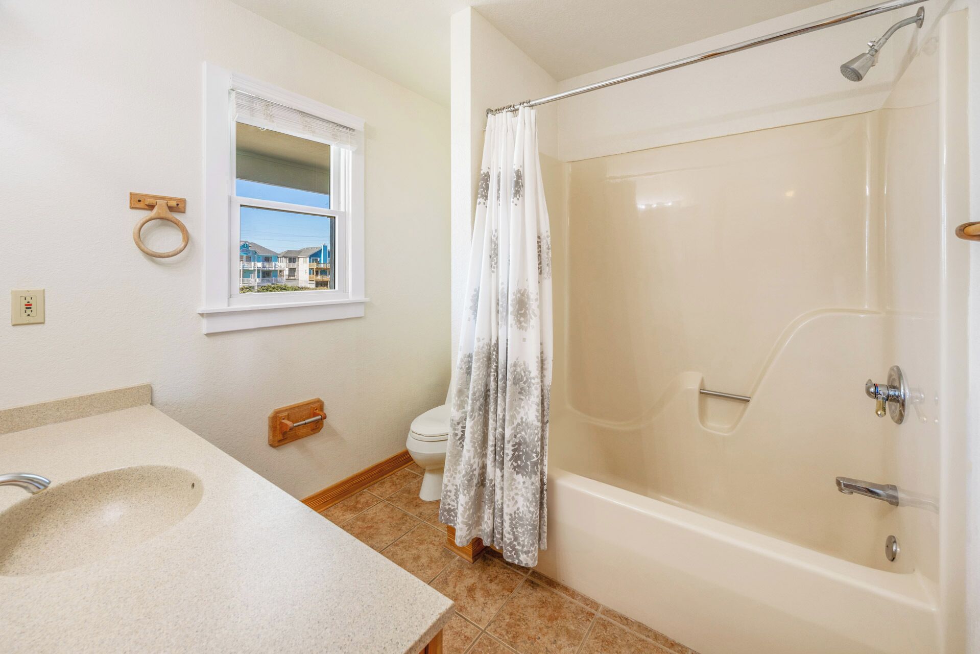 Une salle de bain équipée d’une baignoire, de toilettes, d’un lavabo, d’une fenêtre donnant sur des immeubles et d’un rideau de douche.