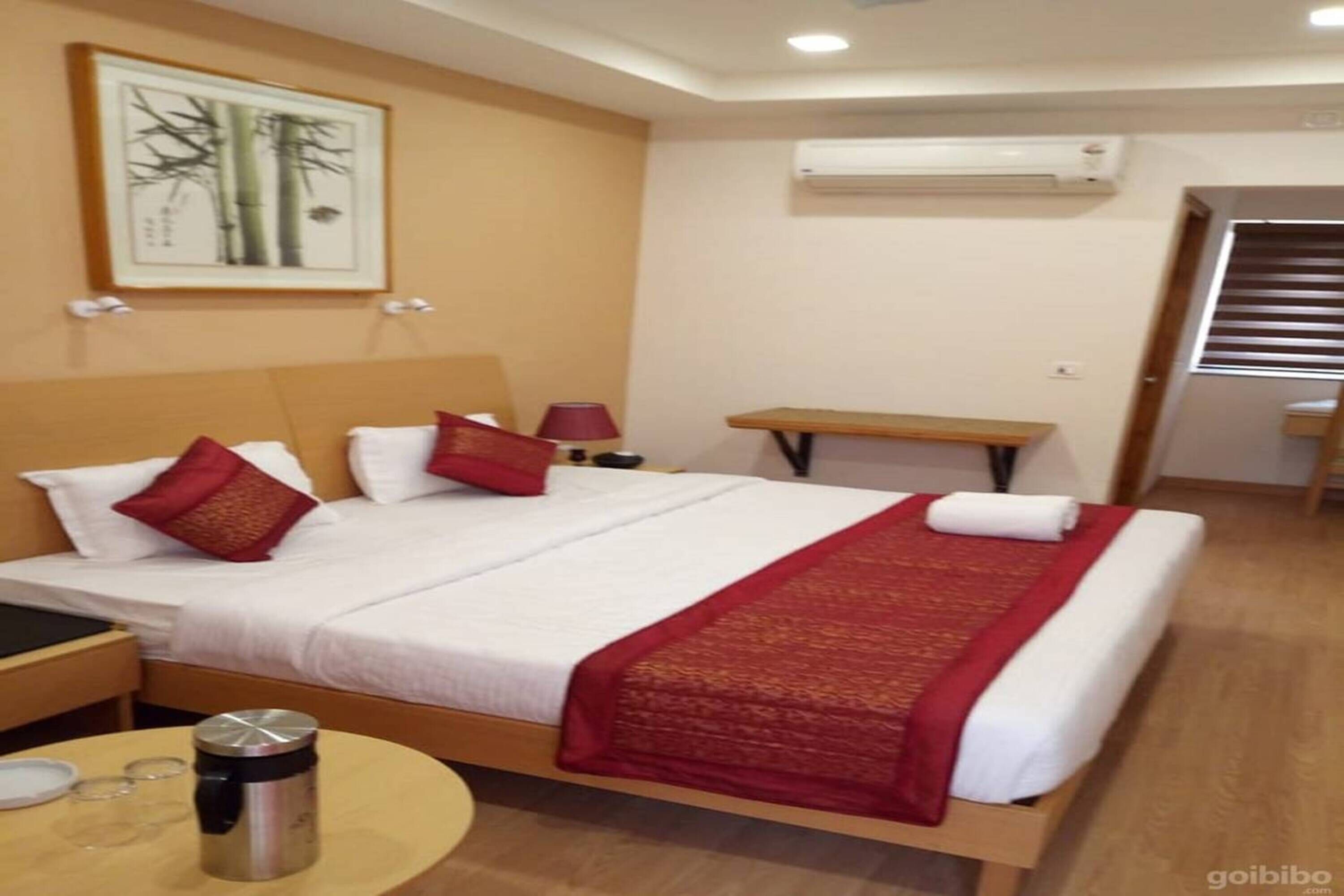 Habitación de hotel con una cama, una mesita de noche, una lámpara, una pequeña mesa con un termo y un equipo de aire acondicionado en la pared.