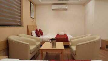 Quarto de hotel com uma cama, duas poltronas, uma mesinha e um aparelho de ar condicionado.