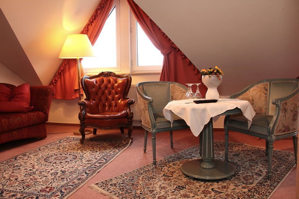 Una habitación acogedora con un sofá rojo, un sillón de cuero y una mesa de comedor con sillas. Una lámpara y un florero con flores están sobre la mesa.