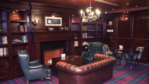 A library with leather armchairs, a fireplace, and bookshelves. - Grand Hotel Victory (Aktau)