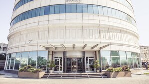 A modern hotel with a curved facade, large glass windows, and a prominent entrance with a revolving door. - Grand Hotel Victory (Aktau)