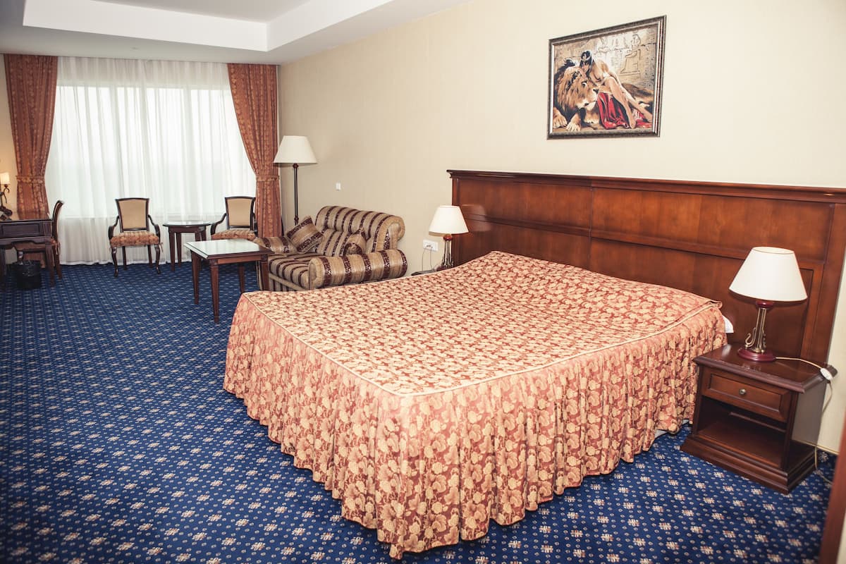 A hotel room with a large bed, two chairs, a small table, and a nightstand with a lamp.