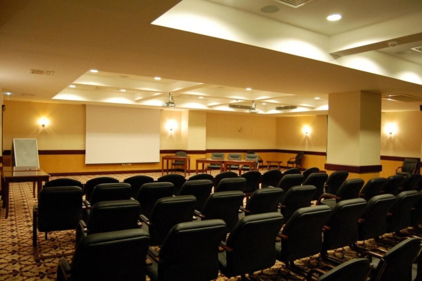 A conference room with rows of chairs, a projector screen, and a table with chairs.