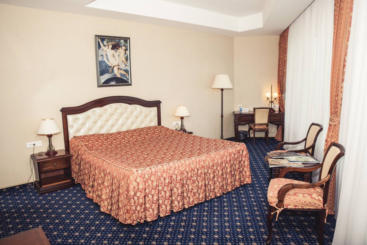 A hotel room with a large bed, two bedside tables with lamps, a desk with a chair, and a painting on the wall.