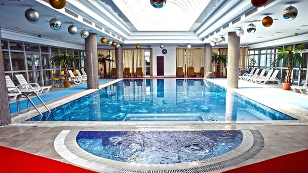 An indoor swimming pool with lounge chairs and potted plants. - Grand Hotel Victory (Aktau)