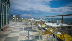 A rooftop terrace with tables and chairs, offering a view of the city and the sea. - Grand Hotel Victory (Aktau)