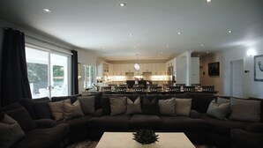 A modern living room with a sectional sofa, a coffee table, and a view of a kitchen and dining area.