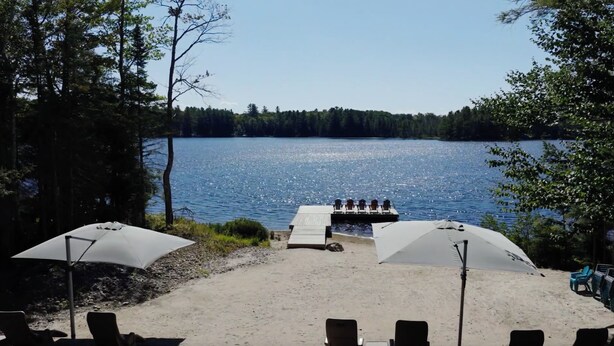 A lakeside view with a dock, chairs, and umbrellas.