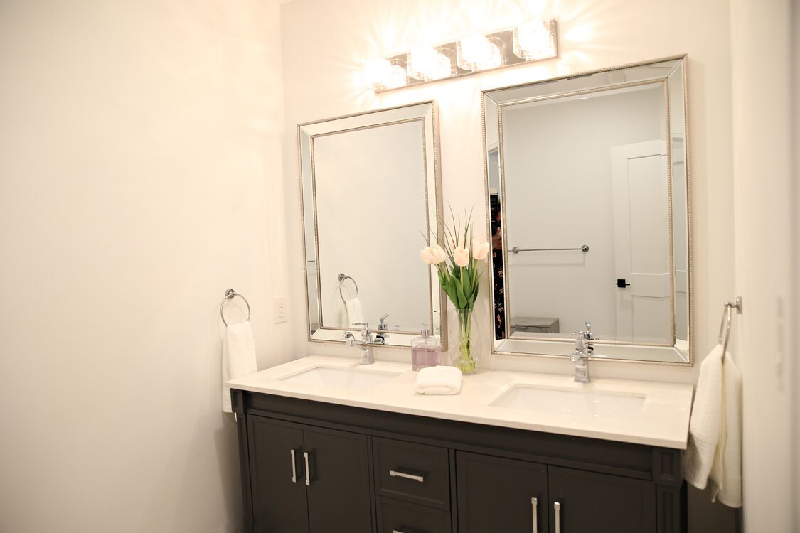 Un baño con dos espejos, un lavabo blanco y un mueble oscuro.