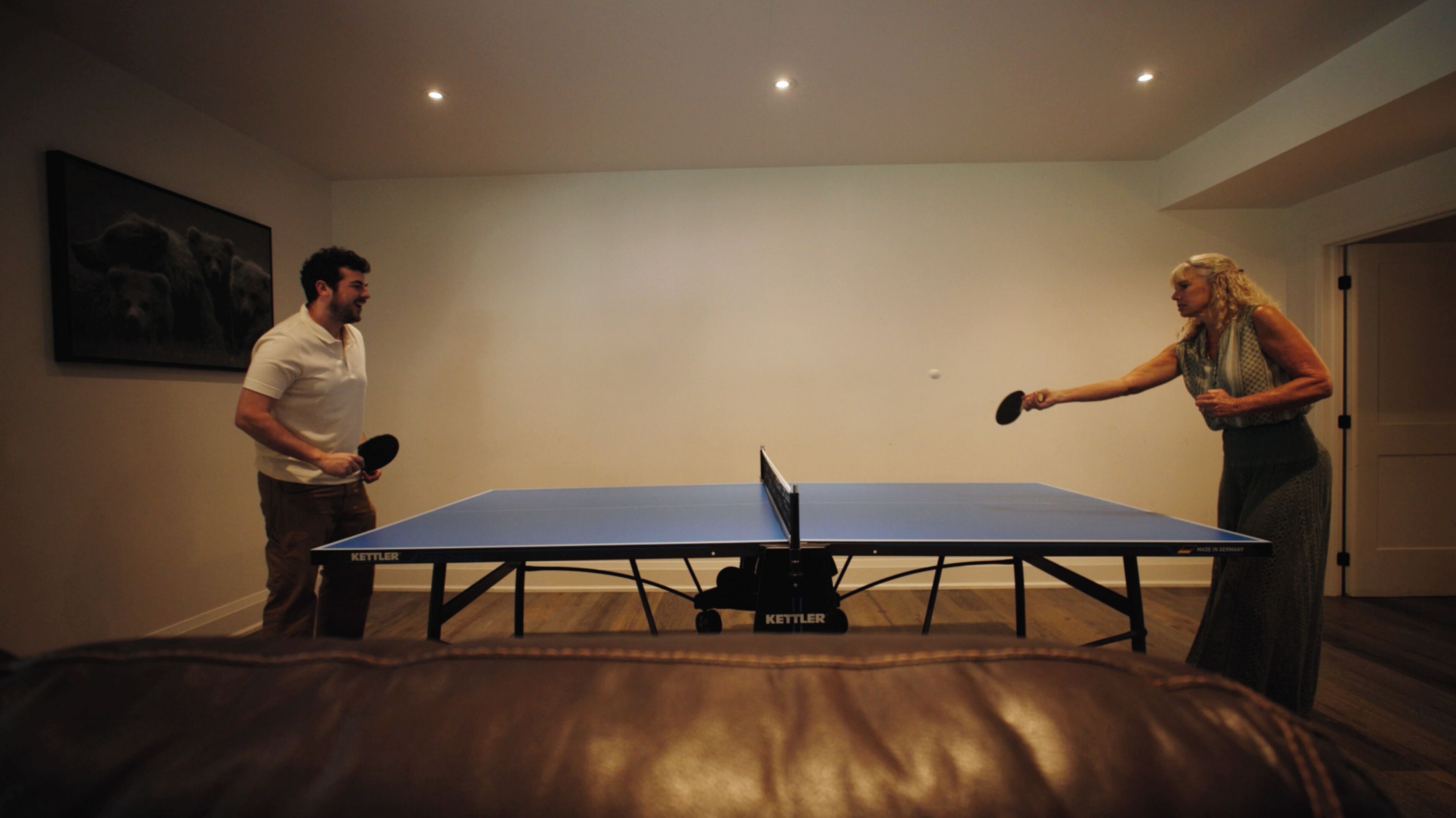 Una habitación con mesa de ping pong, un cuadro en la pared y una puerta.
