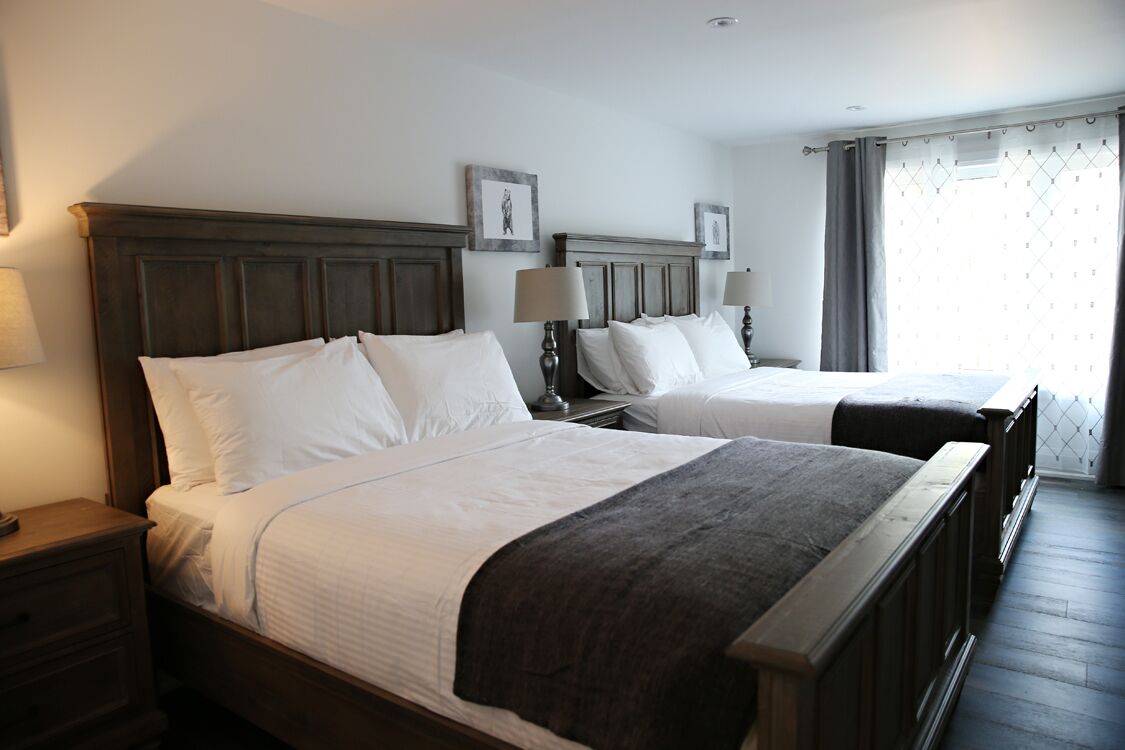 Habitación de hotel con dos camas, cabeceros de madera, lámparas de noche y una ventana con cortinas.