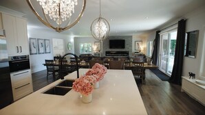 A modern kitchen with white cabinets, a central island with pink flowers, and a chandelier.