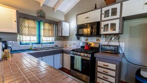 A compact kitchen with a tiled backsplash, a stove, a microwave, and a small countertop. - Lavaughn House - Restorations Tobago (Bon Accord)