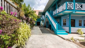 A building with a staircase leading to a balcony, surrounded by tropical plants and a clear sky. - Lavaughn House - Restorations Tobago (Bon Accord)