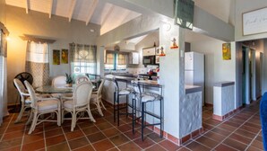 A spacious kitchen with a central island, white bar stools, and a dining area with wicker chairs. - Lavaughn House - Restorations Tobago (Bon Accord)