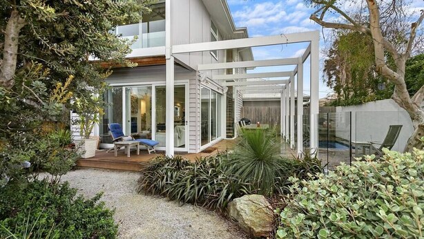 Una casa moderna con un porche cubierto, mobiliario exterior y un jardín bien cuidado.