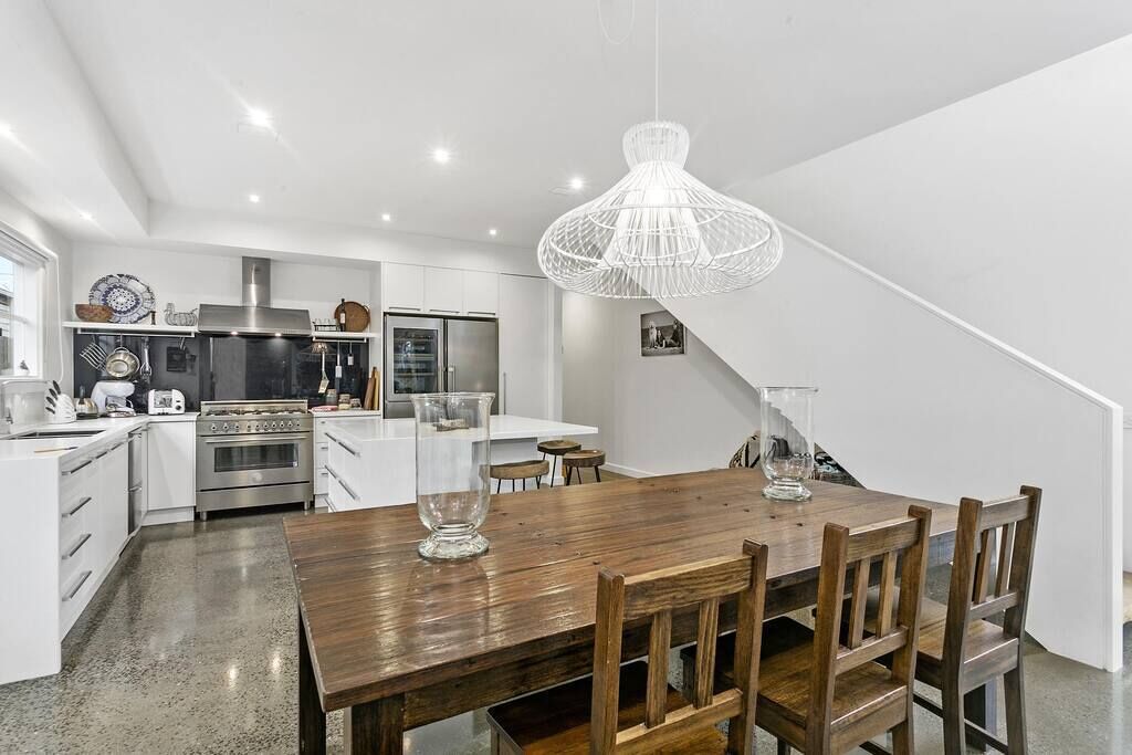 A modern kitchen with white cabinetry, a wooden dining table, and a hanging light fixture.