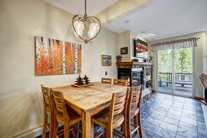 A dining area with a wooden table and chairs, a fireplace, and a view of the outdoors. - Winter Park 4BR — Hot Tub, River Views & Downtown (Winter Park)