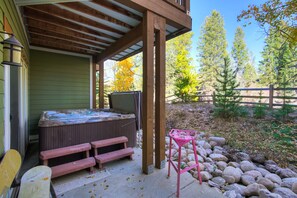 A hot tub under a wooden pergola, wooden benches, and a pink metal table in a garden with a wooden fence and trees. - Winter Park 4BR — Hot Tub, River Views & Downtown (Winter Park)