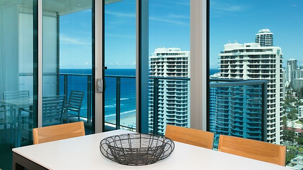 A balcony with a table and chairs, overlooking a cityscape and the ocean. - Orchid Residences' Apartment 22306 redefines luxury (Surfers Paradise)