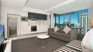 A modern living room with a grey sofa, a round coffee table, and a kitchen area with white cabinets and stainless steel appliances. - Orchid Residences' Apartment 22306 redefines luxury (Surfers Paradise)