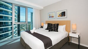 A hotel room with a large bed, two bedside tables, a window with a city view, and two framed pictures on the wall. - Orchid Residences' Apartment 22306 redefines luxury (Surfers Paradise)