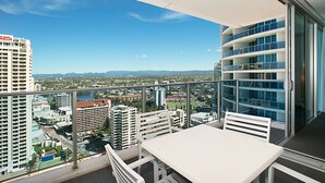 A balcony with a table and chairs, offering a city view with buildings and mountains in the distance. - Orchid Residences' Apartment 22306 redefines luxury (Surfers Paradise)