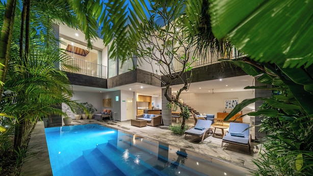 Ein moderner Poolbereich im Innenbereich mit Liegestühlen und einer Treppe, die zu einem Balkon führt.