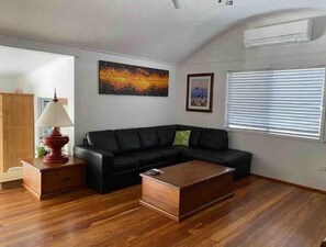 A living room with a black leather sofa, a wooden coffee table, a red lamp, and a painting on the wall.