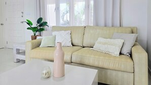Ein Wohnzimmer mit einem beigen Sofa, weißen Kissen, einer Glasvase und einer Topfpflanze.