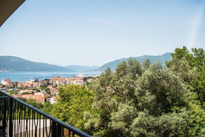 A coastal town with buildings, trees, and a view of the sea and mountains.