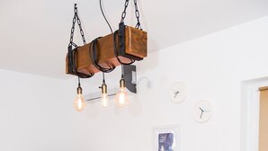 Ruokailutilassa on puinen pöytä, neljä ruskeaa tuolia, riippuvalaisin, seinälle asennettu televisio ja seinäkello.