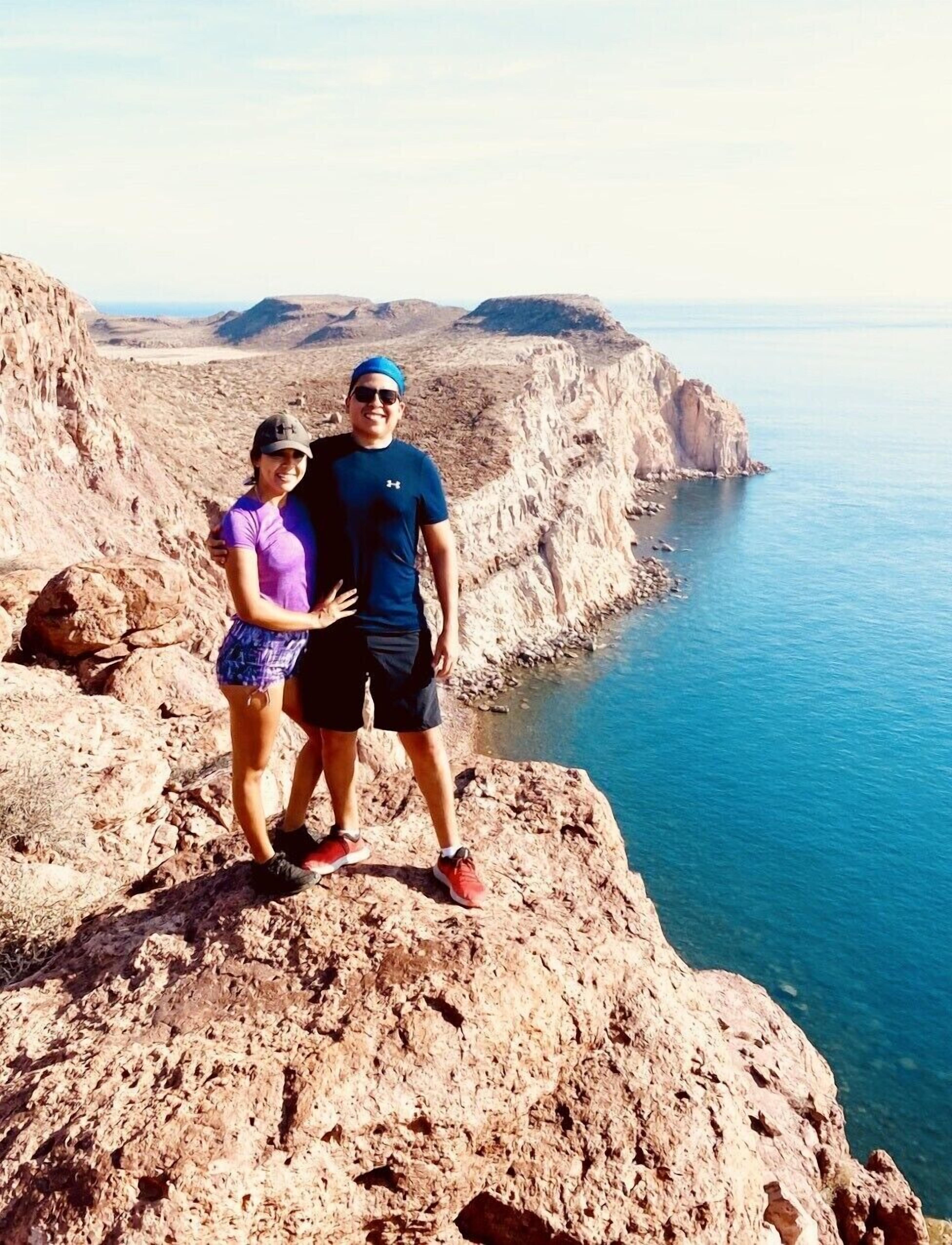 Two people standing on a rocky cliff overlooking a body of water.