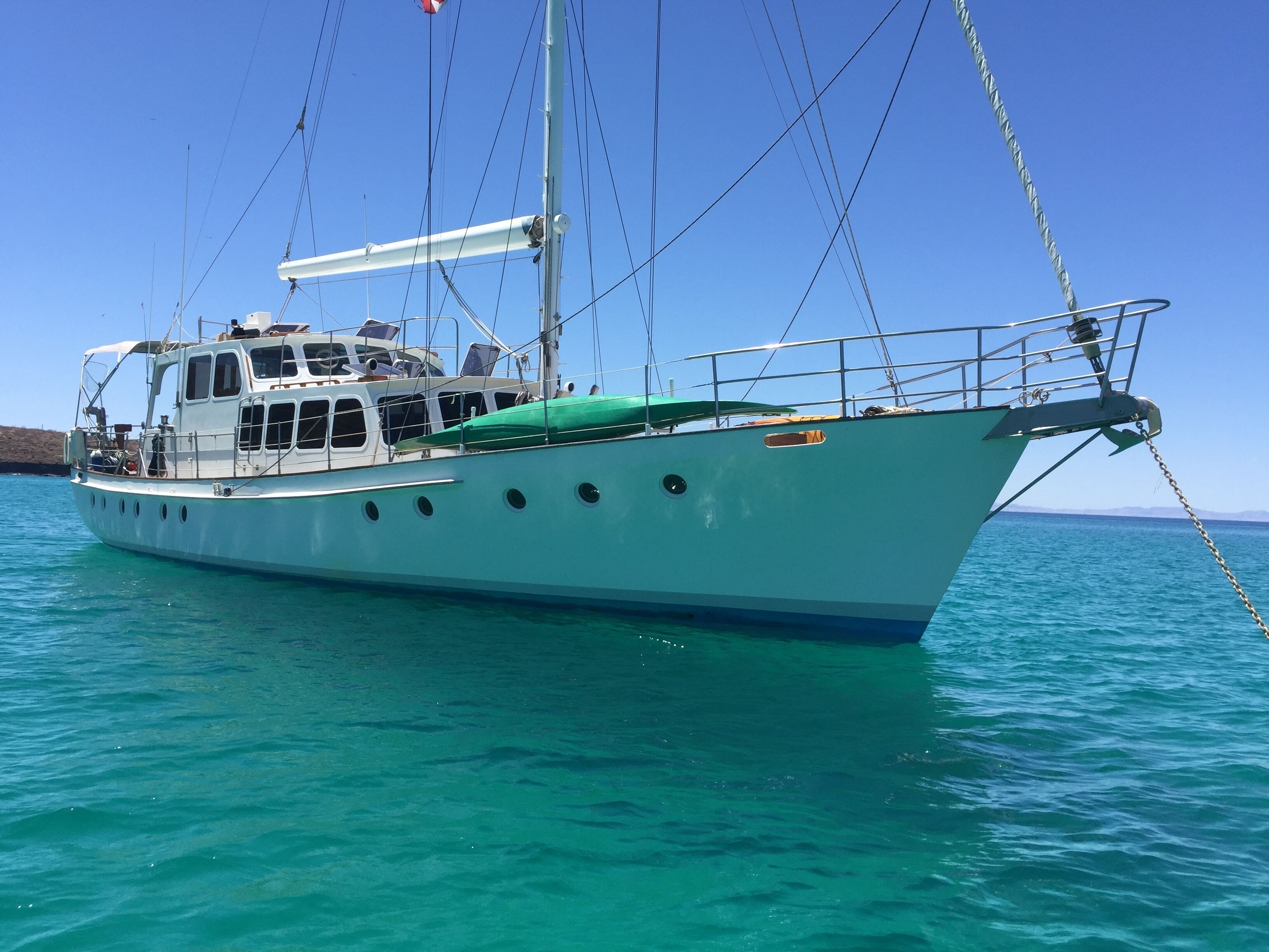 Ein weißes Boot mit Kabine und Deck, vor Anker in klarem, blauem Wasser.