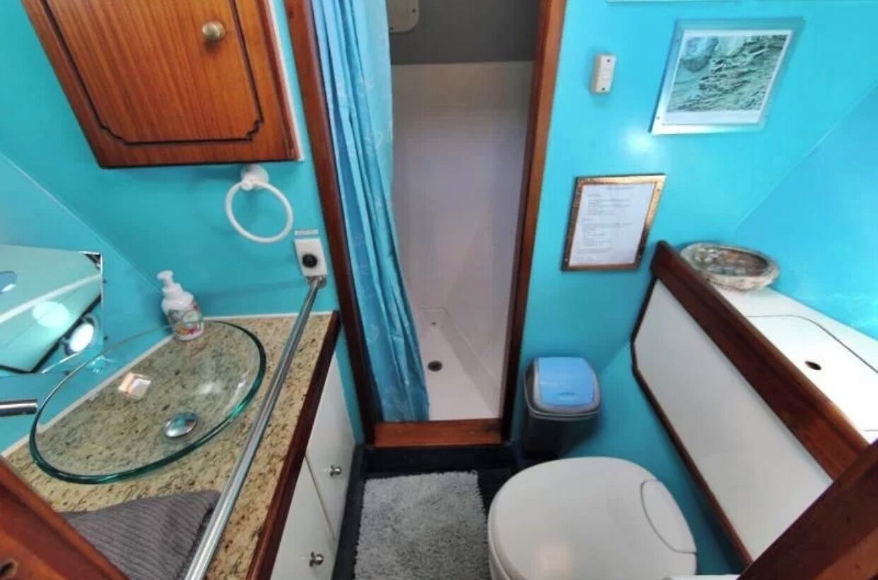 A compact bathroom with a glass sink, a toilet, and a small trash bin.