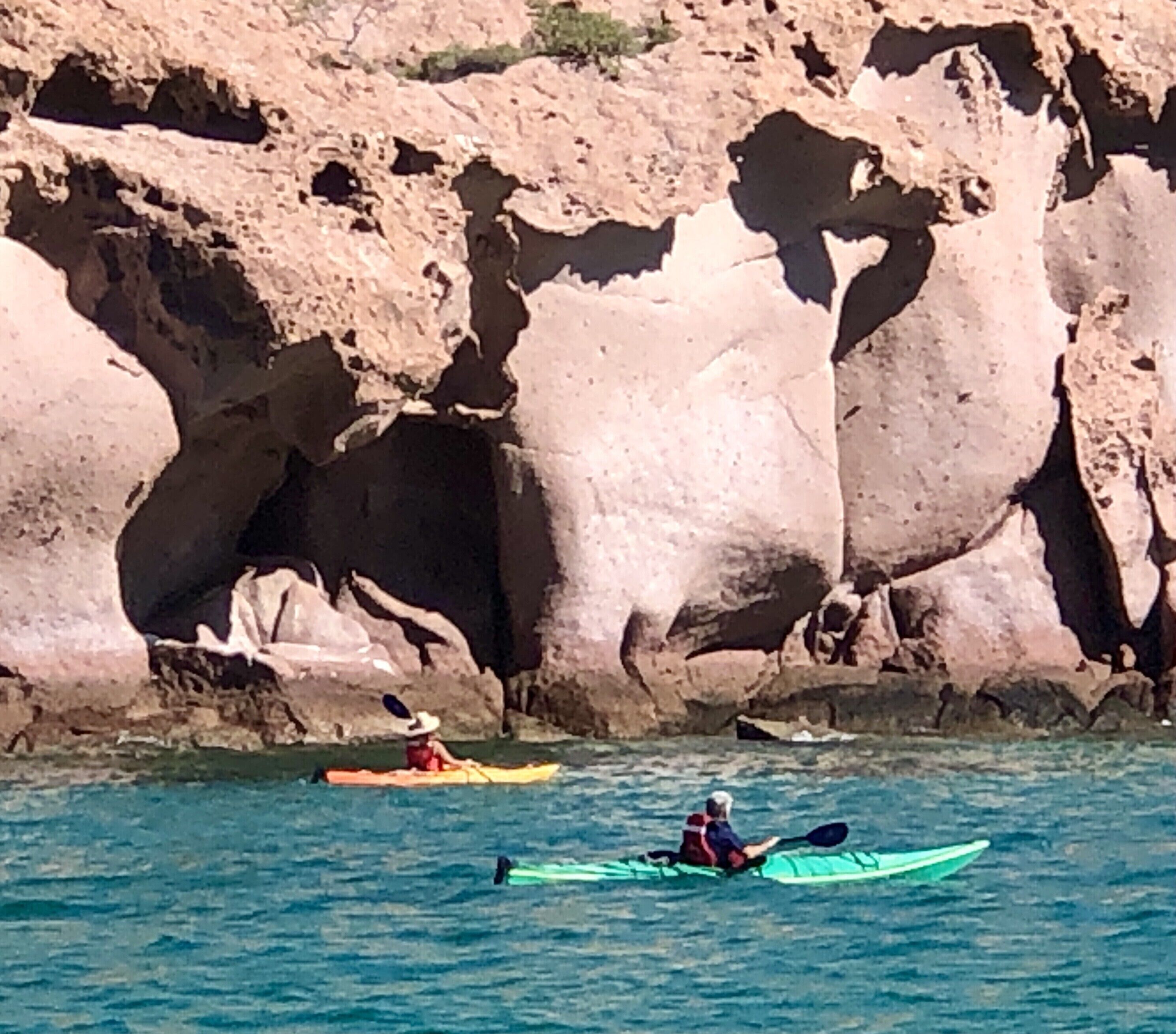 Kayakisti su acque calme, con scogliere rocciose sullo sfondo.