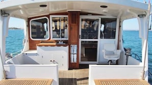 Ein Bootsdeck mit einer zentralen Sitzecke, einer hölzernen Kabinenstruktur und Blick aufs Meer.