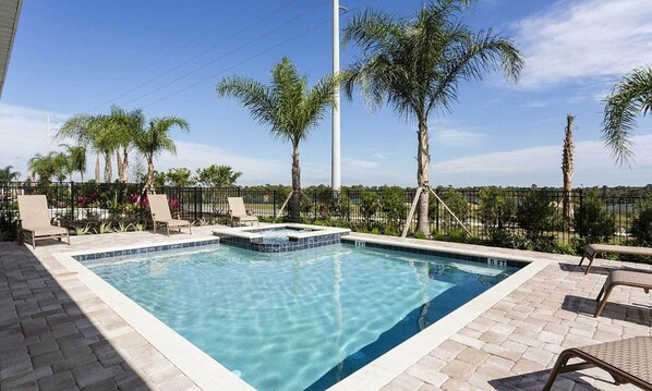 A rectangular pool with a tiled edge, surrounded by lounge chairs and palm trees, with a clear sky in the background. - 10BR Unique Encore Villa | Water Park & Pool (Kissimmee)
