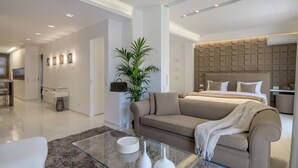 A modern hotel room with a large bed, a sofa, a glass coffee table, and a plant. - Acropolis Amazing Apartment with  Parthenon view (athens)