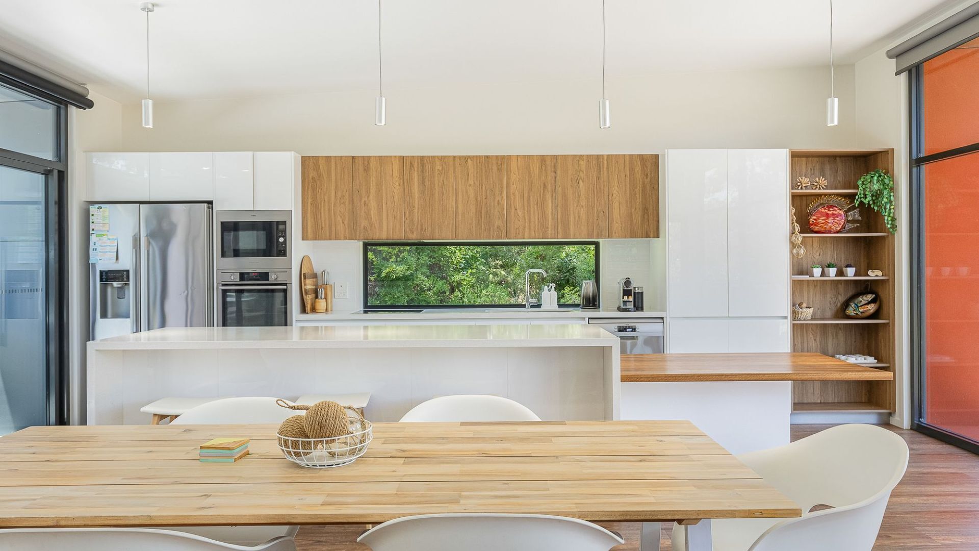 Una cocina moderna con armarios blancos, encimera de madera y vistas a zonas verdes a través del ventanal.